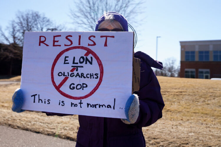 Protester holding up a sign that reads "Resist Elon Tesla Oligarchs GOP This is not normal" outside a Tesla facility in just outside of Minneapolis (Golden Valley) on March 1st, 2025. This is the third weekend in a row they've gathered to protest the actions of Elon Musk and the current administration Protester holding up a sign that reads "Resist Elon Tesla Oligarchs GOP This is not normal" outside a Tesla facility in just outside of Minneapolis (Golden Valley) on March 1st, 2025. This is the third weekend in a row they've gathered to protest the actions of Elon Musk and the current administration